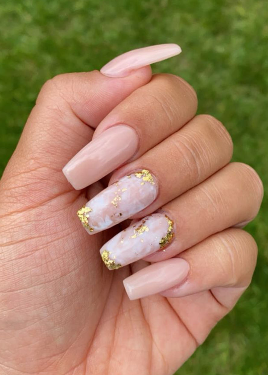Lange nude nagels, twee met roze marmer en bladgoud, tegen een groen gazon
