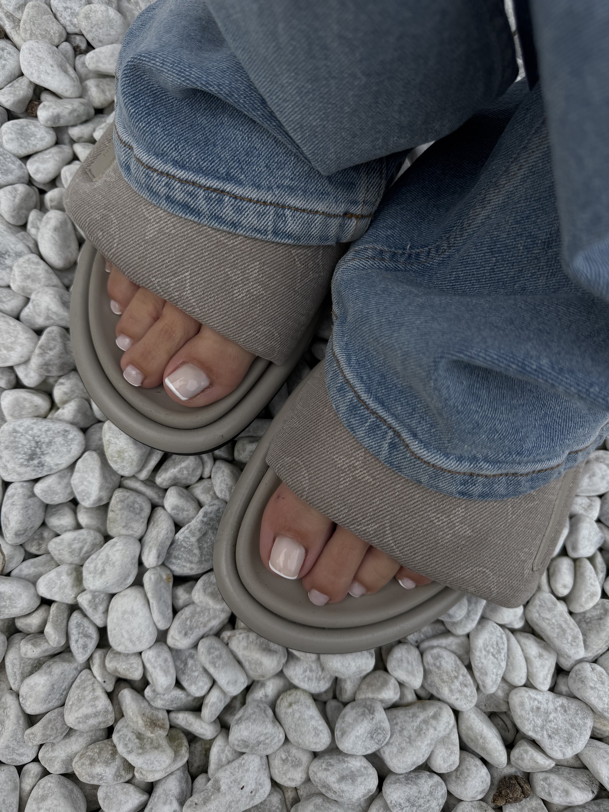 Verzorgde voeten met nude teennagels, in slippers op witte kiezels